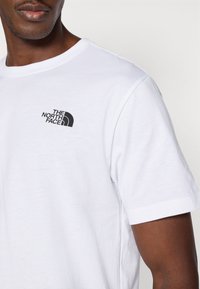 Λευκό βαμβακερό t-shirt με κοντά μανίκια, με μαύρο λογότυπο "The North Face" στην αριστερή πλευρά του στήθους. Απλός σχεδιασμός και λεία υφή.