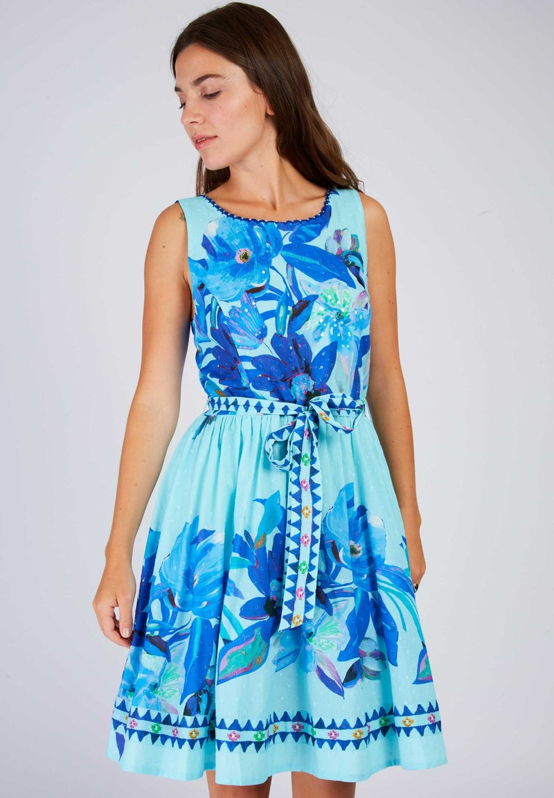 Ein ärmelloses, A-Linien-Kleid in Hellblau mit großen blauen Blumenmustern, einem gewellten Ausschnitt und einer gebundenen Taille mit spitzen Akzenten.