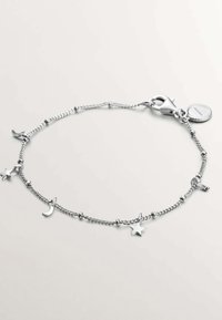 Pulsera de cadena de plata con charms de estrella y luna creciente, con un cierre de langosta y una pequeña etiqueta circular. Acabado de metal pulido.
