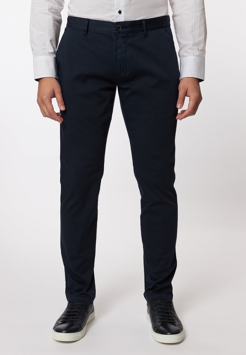 Navy Chinos aus gewebtem Stoff, im Slim Fit-Stil, mit vorderen Taschen und einem Knopfverschluss, kombiniert mit schwarzen Sneakern.