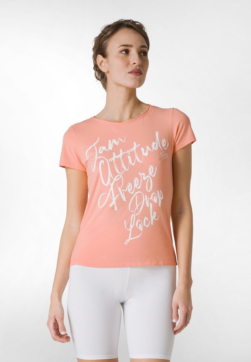 Ferskenfarvet bomulds T-shirt med korte ærmer, der prydes af hvid grafisk tekst, kombineret med hvide tætsiddende shorts. Glat tekstur, klassisk crew neck design.