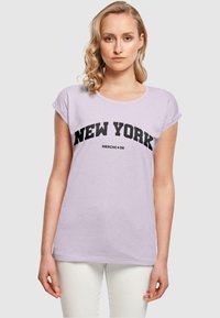 Lys lavendel t-shirt med korte oprullede ærmer, prydet med fed sort "NEW YORK" tekst og lille "MERCHCODE" logo nedenfor. Blødt bomuldsstof.