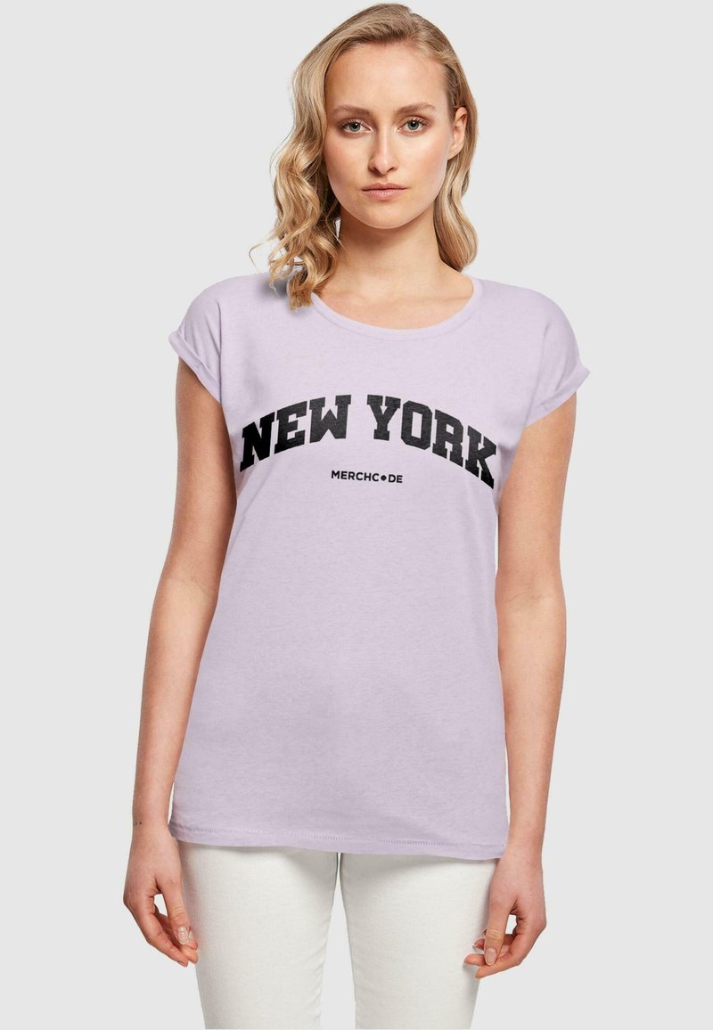 Lys lavendel t-shirt med korte oprullede ærmer, prydet med fed sort "NEW YORK" tekst og lille "MERCHCODE" logo nedenfor. Blødt bomuldsstof.