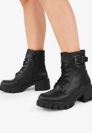 Botas de cuero negro hasta el tobillo con suela gruesa, cierre de cordones en la parte delantera, cremallera lateral y un detalle de correa con hebilla. Textura suave con un diseño robusto.