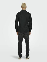 Zwarte lange mouwen shirt van gladde stof, met geknoopte manchetten en een gestructureerde kraag, gecombineerd met donkergrijze jeans en witte sneakers.