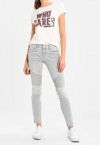 White graphic t-shirt with "WHO CARES" in bold black and red letters, paired with light gray skinny jeans featuring ribbed accents and white sneakers.