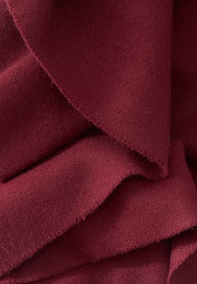 Tissu doux plié avec une texture lisse dans une couleur bordeaux foncé, montrant des bords superposés et des ombres subtiles.