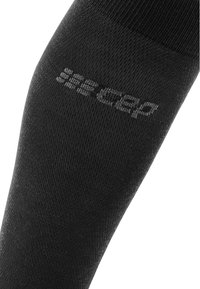 Calza compressiva nera con una texture liscia. Presenta un logo stampato in una tonalità più chiara sul tessuto. Design aderente per supporto.