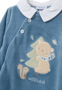 Conjunto de bebé de terciopelo azul con cuello blanco, diseño bordado de oso y árbol, y detalle de ardilla cerca del dobladillo. Cierres de botones en la parte delantera.