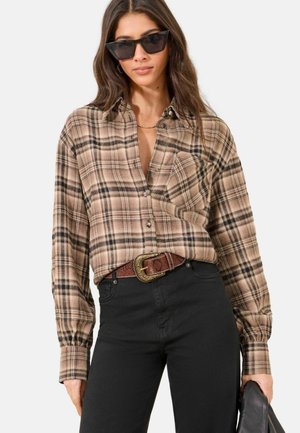 Woman wearing brown plaid button-up shirt, black high-waist pants with brown belt, black sunglasses, holding a black clutch bag.