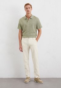 Green speckled polo shirt with three buttons, paired with cream-colored trousers and beige shoes. Simple design with a relaxed fit.