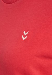 Czerwony bawełniany T-shirt z okrągłym dekoltem i białym, abstrakcyjnym haftem logo na górnej lewej stronie. Gładka tekstura, dopasowany krój.