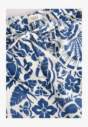 Tissu en lin blanc avec un motif floral bleu, doté d'une taille élastique et d'un ruban noué. L'étiquette indique "next contient du lin."