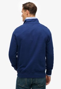 Sudadera azul marino con cuello alto, puños y dobladillo acanalados. Fabricada con un material suave, presenta una textura lisa sin patrones visibles.