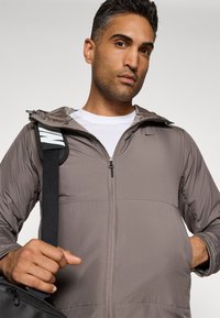 Lätt grå zip-up jacka med huva och dragkedjefickor, med subtil sömnad och en liten logotyp på bröstet.