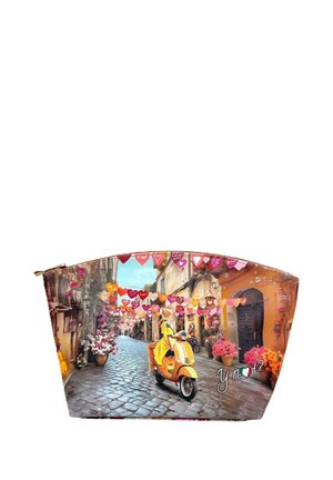 Una donna con un vestito e cappello gialli guida uno scooter giallo lungo una strada lastricata decorata con ornamenti colorati a forma di cuore appesi.