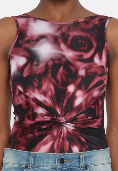 Top sin mangas con un estampado floral en negro y burdeos, con un detalle frontal retorcido y una textura suave. Combinado con jeans de mezclilla azul claro.