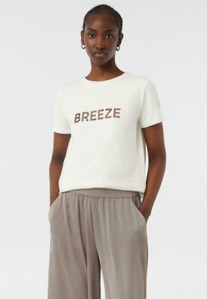 Helles beige T-Shirt mit kurzen Ärmeln und braunem Text "BREEZE" auf der Vorderseite, kombiniert mit locker sitzenden taupefarbenen Hosen mit Seitentaschen.