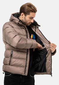 Pufferjacke in Taupe mit gestepptem Textil, Reißverschlusstaschen und abnehmbarer Kapuze. Schwarze Fütterung im Inneren der Jacke sichtbar.