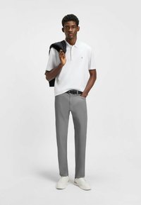 White polo shirt with collar, gray trousers, and white sneakers. Black sweater draped over shoulder. Simple, casual design with minimal accents.