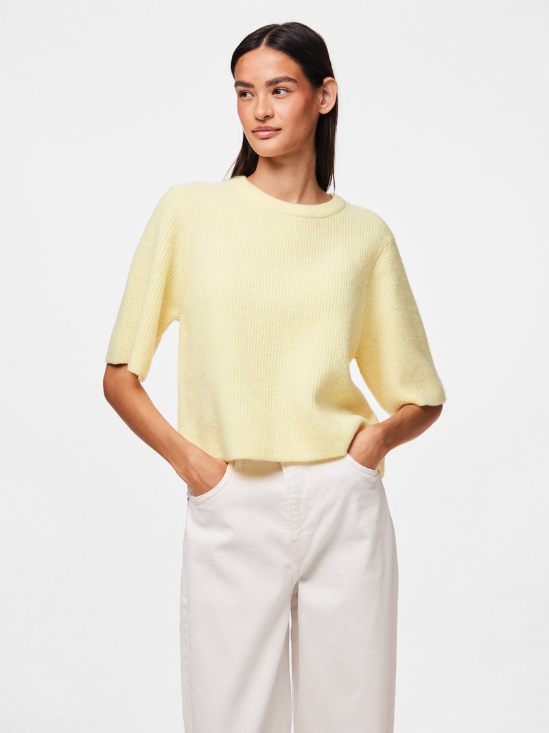 Yellow ribbed knit sweater with a rounded neckline and short sleeves, paired with light-colored straight-leg pants. Textured fabric.