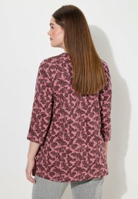 Maglietta rosa a maniche lunghe con un motivo floreale in marrone scuro. Realizzata in tessuto morbido, presenta un orlo arrotondato e maniche a tre quarti.
