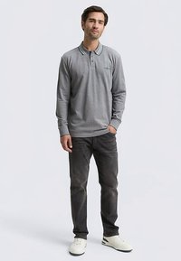 Pilkas ilgomis rankovėmis polo marškinėlis su žaliai balta dryžuotu apykakliu, derinamas su tamsiomis džinsinėmis kelnėmis ir baltais batais. Modelis stovi neutrali poza.