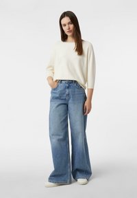 Kremowy sweter z długimi rękawami w połączeniu z jasnoniebieskimi szerokimi spodniami jeansowymi. Strój cechuje się luźnym krojem i prostym designem.