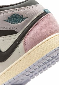 Κοντινή λήψη της φτέρνας ενός αθλητικού παπουτσιού Air Jordan σε ροζ, γκρι και λευκό σουέτ, με ανάγλυφη κρεμ σόλα και ανάγλυφο λογότυπο με φτερωτό μπάσκετ.