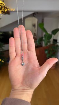 Silberne Halskette, die auf einer Hand präsentiert wird, mit einer filigranen Kette und einem kleinen, flammenförmigen Anhänger mit detailreicher Verzierung.