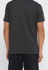 Camiseta de manga corta gris oscuro hecha de tela suave, con un corte recto, aberturas laterales y un cuello redondo clásico.