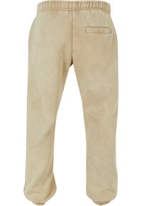 Beige joggebukser med elastisk linning og mansjetter, med en enkelt baklomme og en glatt, litt teksturert overflate.
