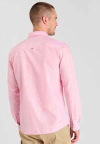 Camicia a maniche lunghe di colore rosa chiaro con righe bianche, dotata di colletto a punta e un piccolo logo nella parte superiore della schiena. Tessuto in cotone.