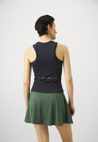 Navy tank top with racerback design, paired with a green flared skirt. The tank features a logo band at the waist. Smooth fabric texture.