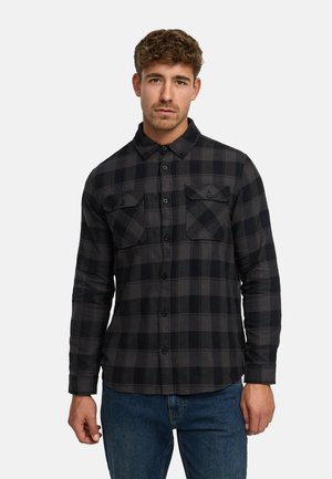 Svart og grå rutete flanellskjorte med lange ermer, knappelukking foran, krage og to brystlommer. Brukt sammen med blå denimjeans.