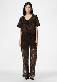 Brun blondebluse med korte ermer, har knytebånd foran; matchende brune blondebukser med gjennomsiktige paneler, pyntet med blomsterdesign.