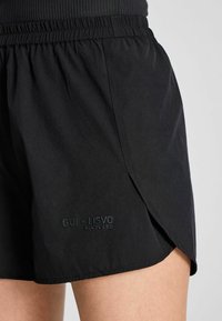 Zwarte shorts van gerecycled materiaal, met een elastische tailleband, zijslitsen en een reliëflogo detail nabij de zoom.