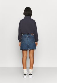 Pull-over bleu marine à col montant, associé à une jupe en jean. La jupe comporte des poches arrière et un ourlet effiloché. Des chaussettes blanches et des baskets complètent le look.