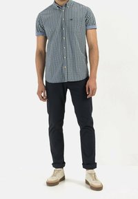 Camicia a maniche corte a quadri blu navy e bianca, con colletto button-down e maniche arrotolate, abbinata a pantaloni scuri e sneakers casual.