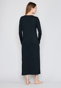 Długa sukienka z długim rękawem w intensywnie czarnym kolorze, z bocznymi rozcięciami, wykonana z gładkiej tkaniny, z okrągłym dekoltem i luźnym fasonem.