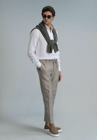 Chemise légère en lin blanc, écharpe en tricot gris clair, pantalon beige rayé et chaussures gris avec semelles blanches.