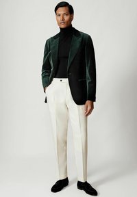 Roheline sametbleiser mustade aktsentidega, millele on lisatud kreemjad püksid ja mustad kingad. Kitsas lõige ja ühtlane pind kogu ulatuses.