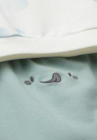 Světle modrá a bílá bavlněná mikina se mátově zelenou spodní stranou, s malým vyšitým motivem usmívající se tváře.