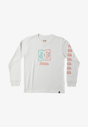 Biała bluzka z długim rękawem z kolorowym graficznym logo na piersi oraz powtarzającym się napisem na rękawach, połączona z jasnoniebieskimi dżinsami i trampkami.