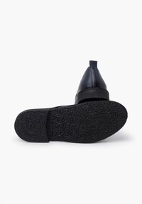 Scarpa in pelle nera con suola in gomma texturizzata. Il design presenta un tacco basso e una linguetta sul retro per facilitare l'indossamento.
