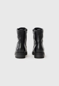 Botas de tobillo de cuero negro con una textura suave, cremallera lateral y suela de goma resistente. Detalles de costura a lo largo de la parte trasera y los laterales.