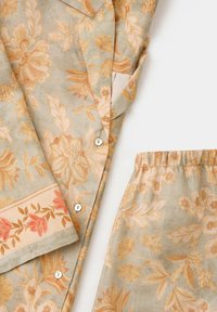 Ensemble de pyjama floral beige clair avec motifs de fleurs pêche et orange, chemise boutonnée et pantalon à taille élastique sur fond blanc.