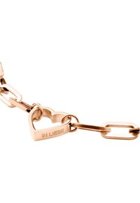 Bracciale a catena in oro rosa con anelli piatti ovali e a forma di cuore interconnessi. L'anello a forma di cuore è inciso con "IN LIEBE". Texture liscia, design minimalista.