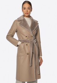 Heller Ledercoat mit Doppelreiher-Design, großem Pelzkragen, seitlichen Taschen und einem gebundenen Taillengürtel. Glatte Oberfläche mit dezentem Glanz.