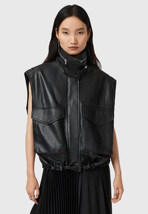 Gilet senza maniche in pelle nera con colletto alto, dotato di chiusura frontale con zip e due tasche a toppa. Tessuto testurizzato con dettaglio a fondo arricciato.